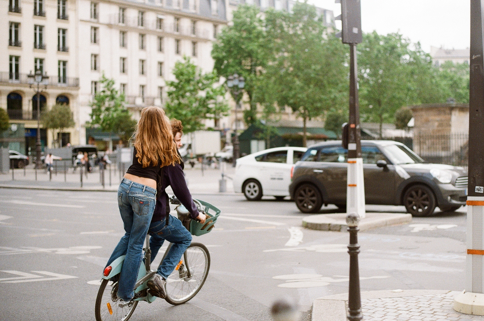 Two people ride a bicycle on a city street.