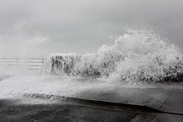 A black-and-white image of a wave breaking over a seawall.