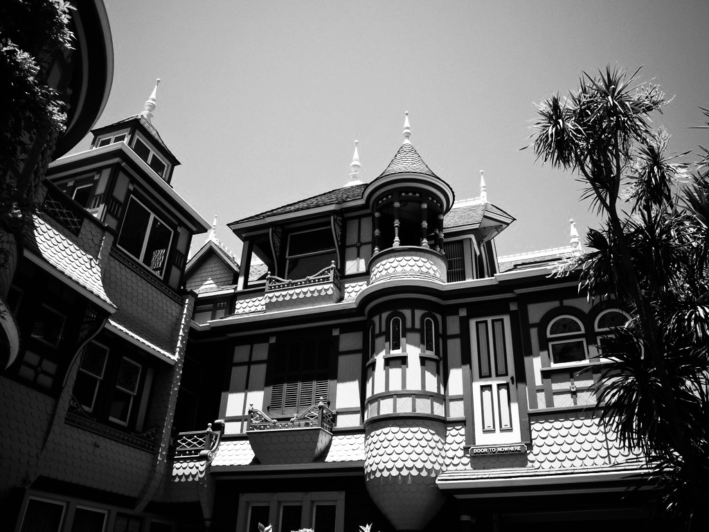 This is a black-and-white photograph, a partial view of a Victorian house with ornate spires and a gray sky beyond.